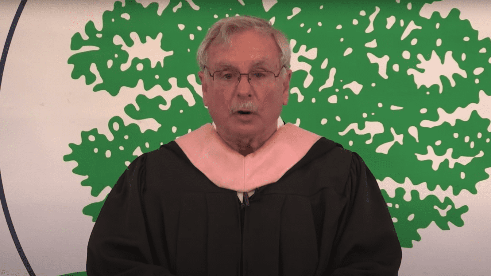 man standing at podium in black robe at graduation