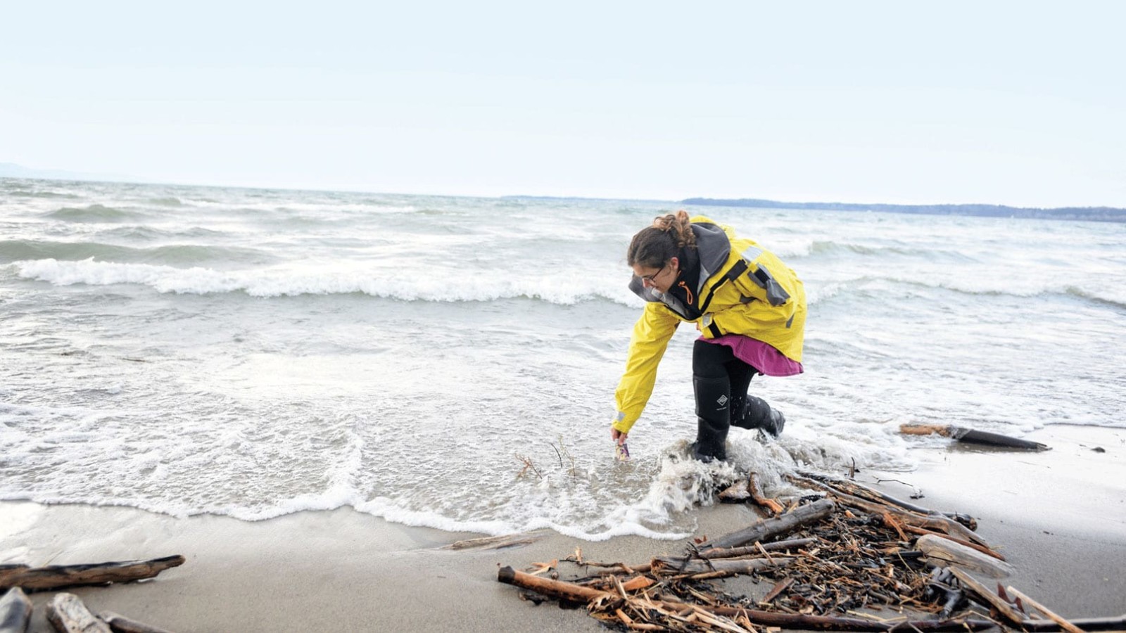 Woman in yellow coat standing in shallow ocean water