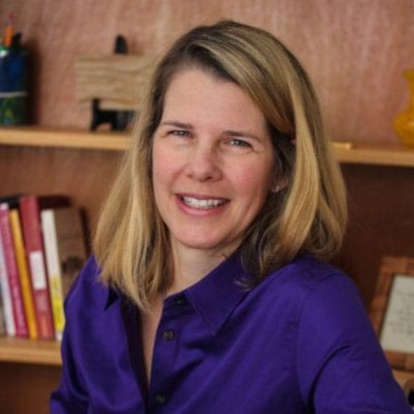 Person smiling in purple shirt in front of book shelf