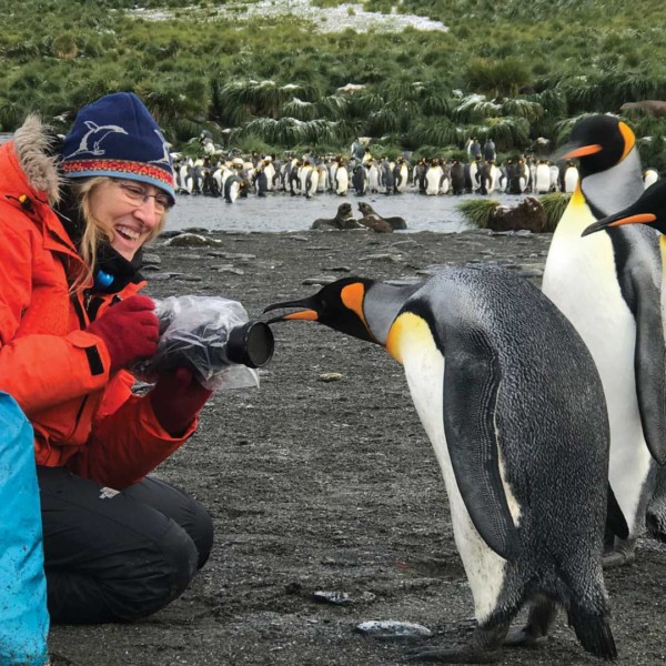 woman in hat and coat with penguin pecking at camera