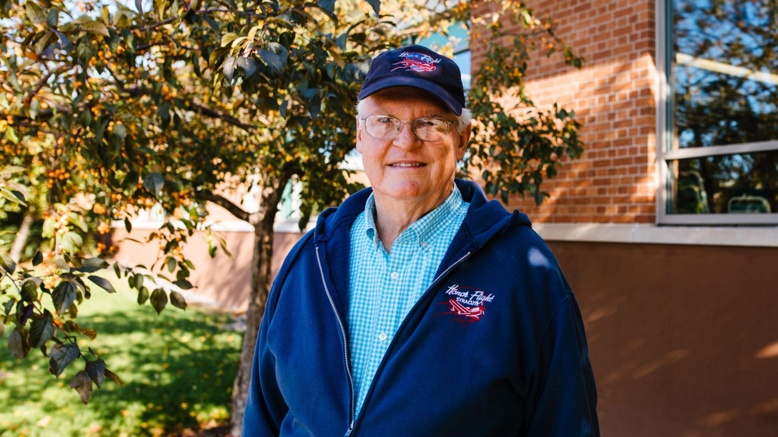 man with glasses in baseball hat in front of brick building