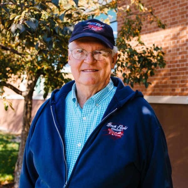 man with glasses in baseball hat in front of brick building