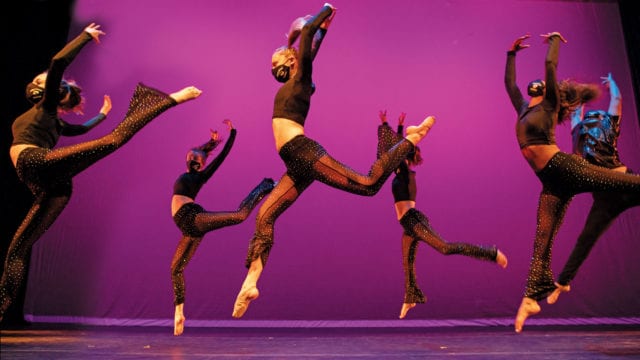 dancers leap across a stage with dark pink background