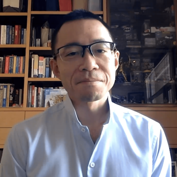 Man in glasses speaking in front of a bookcase