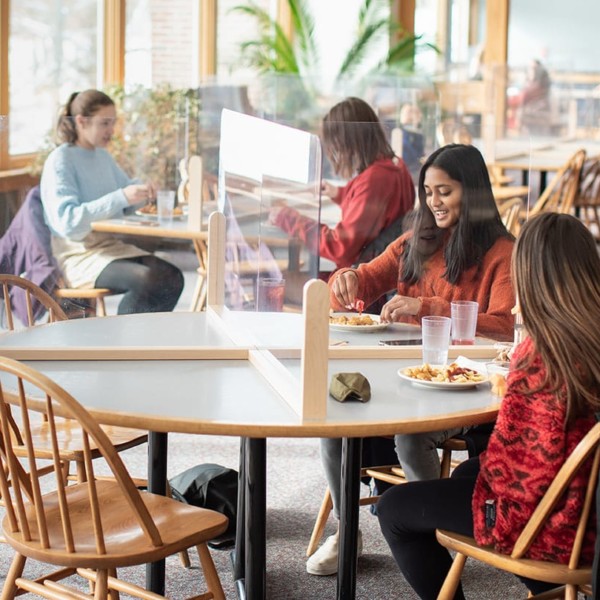 students eating lunch at tables with plexiglass dividers pandemic