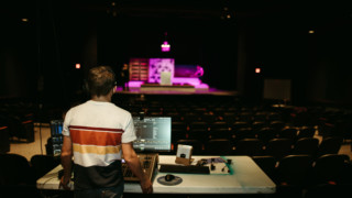 student at sound board in theater booth