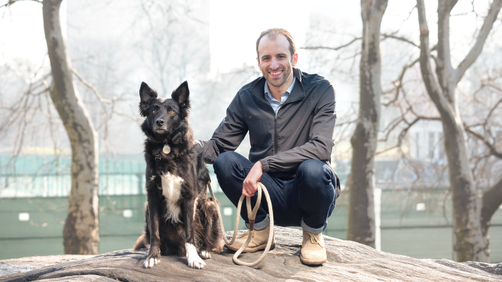 man crouches in Central Park with dog