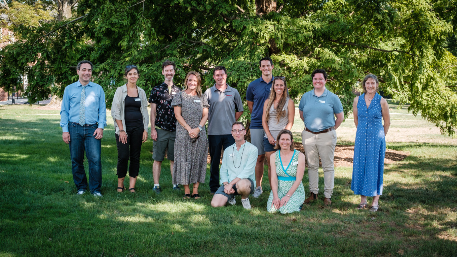 11 adults pose outside in the shade of a tree