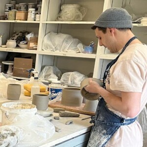 student works on ceramics piece as students observe