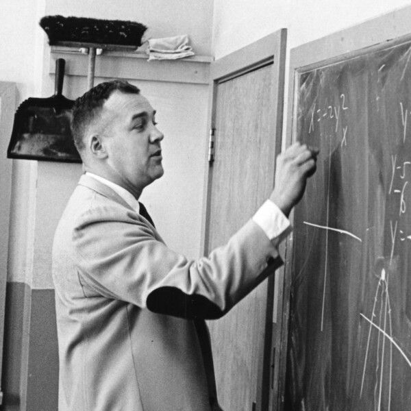 black and white photo of teacher in sportcoat at blackboard