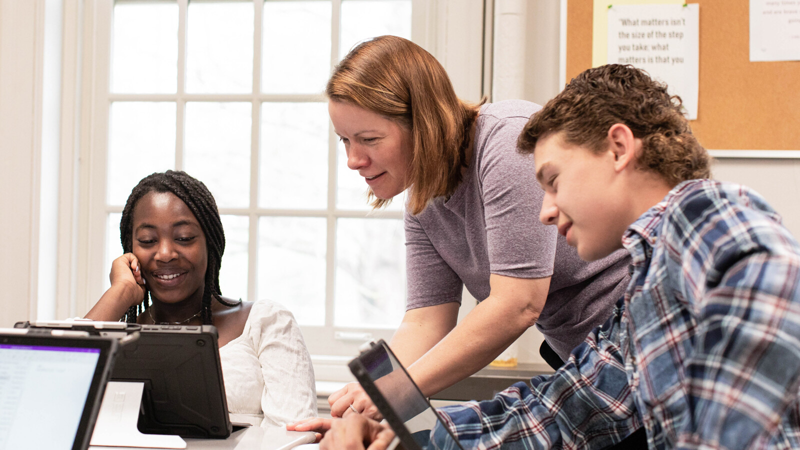 teacher looking at computer with students in classroom