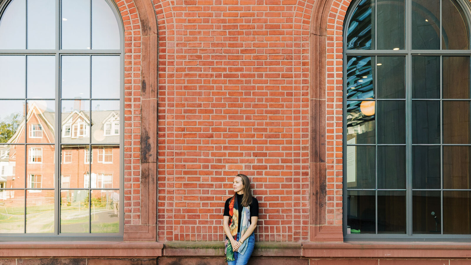 Woman standing against brick wall between two windows