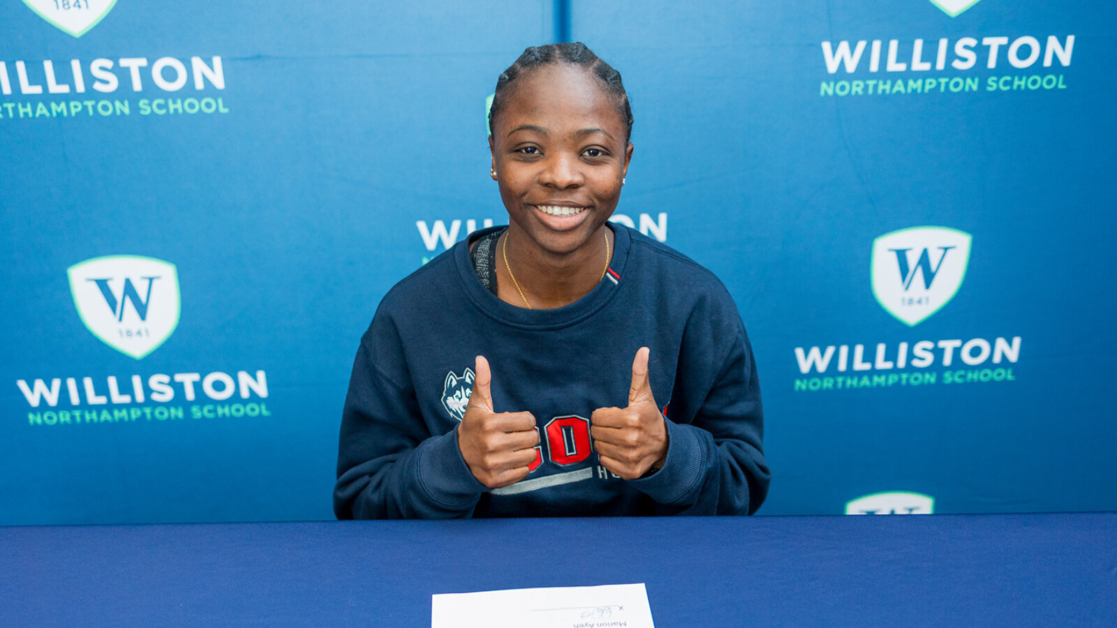 Student giving two thumbs up on school backdrop