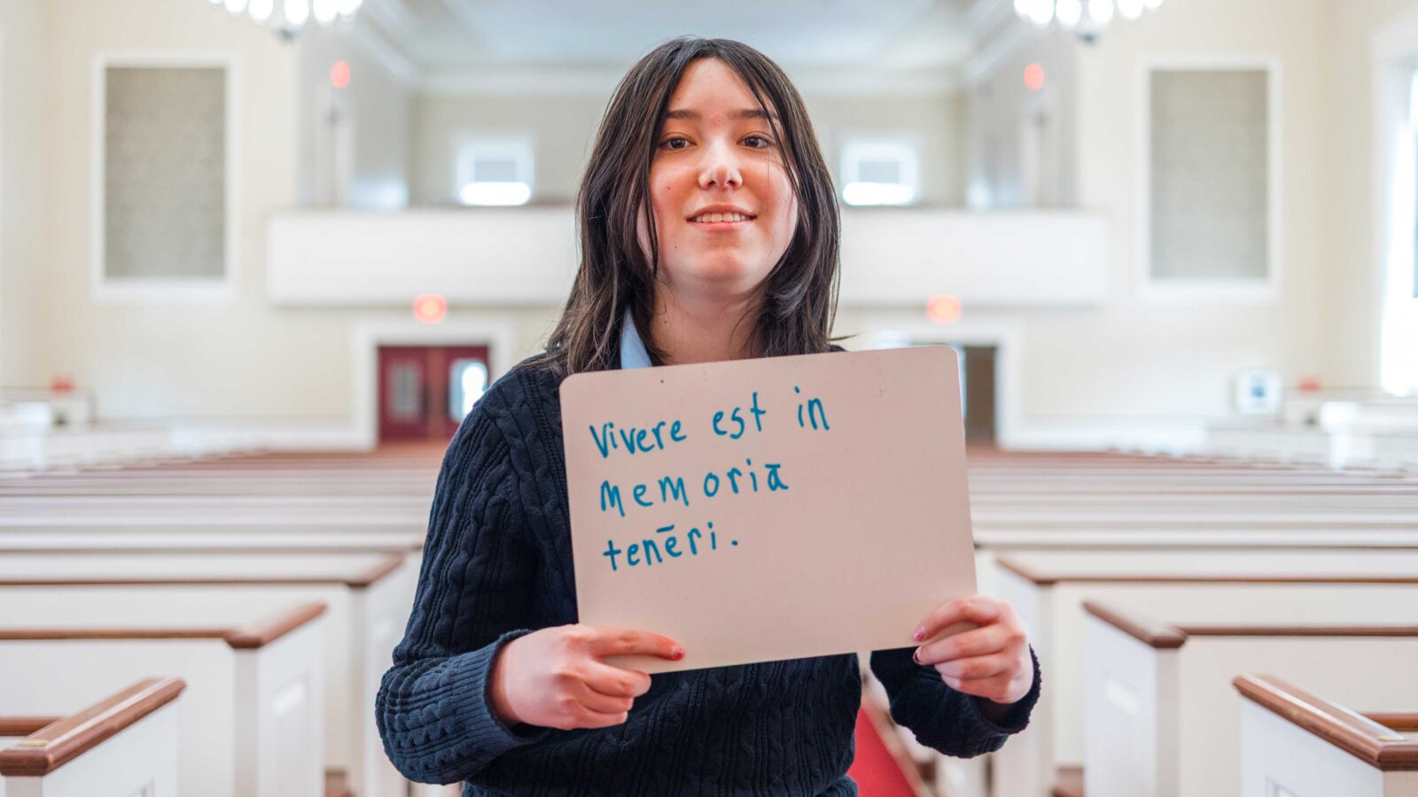Latin student holds up sign in Phillips Stevens Chapel with award-winning quote written on it