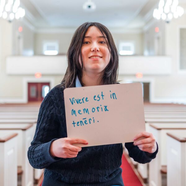 Latin student holds up sign in Phillips Stevens Chapel with award-winning quote written on it