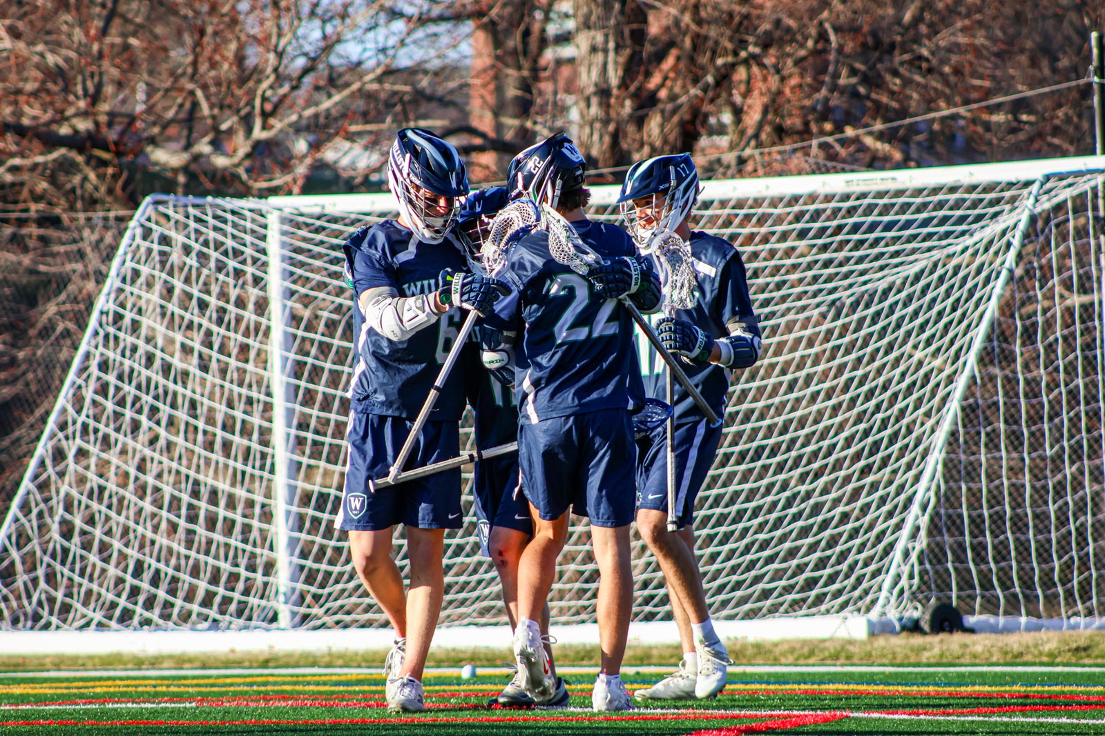 Four varsity boys lacrosse players celebrate after a goal