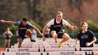Three boys track athletes compete in a hurdles event