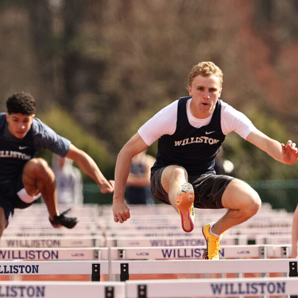 Three boys track athletes compete in a hurdles event