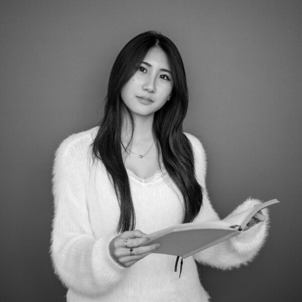 black and white photo of student holding notebook, looking at the camera
