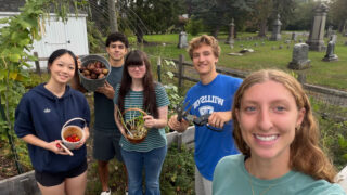 five students hold up vegetables picked from the community garden