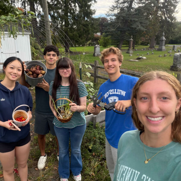 five students hold up vegetables picked from the community garden