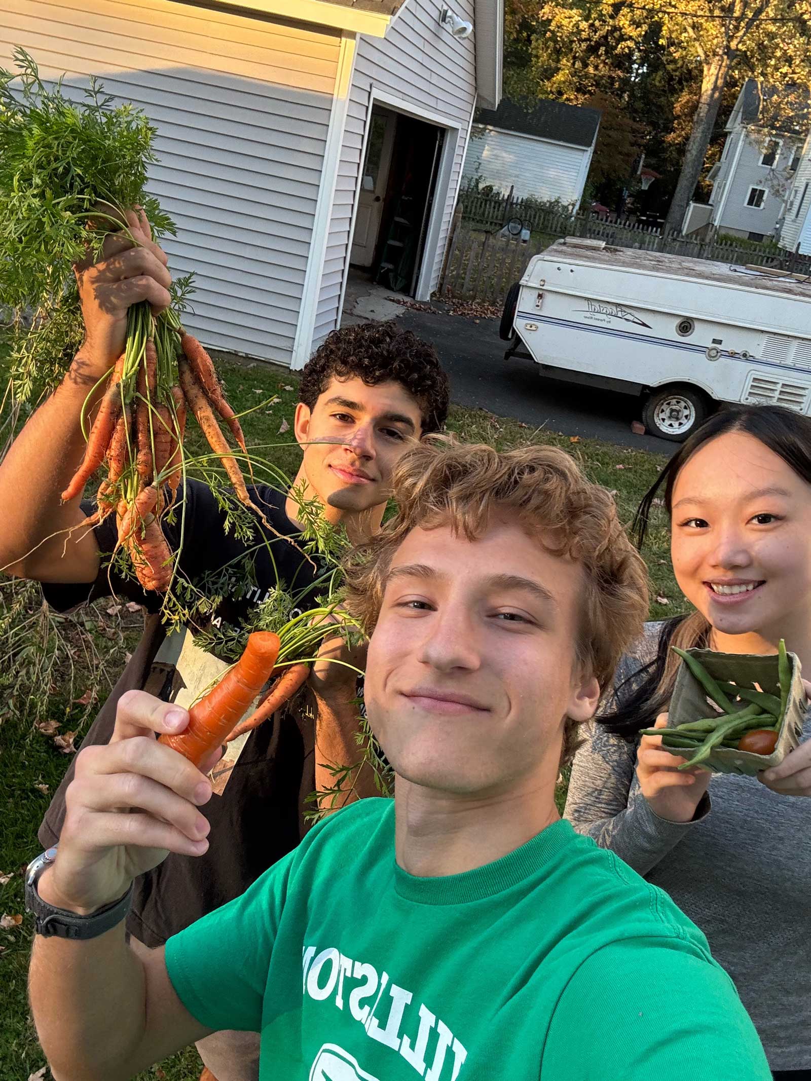 Three students hold up vegetables harvested from the community garden